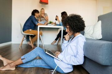 Wall Mural - Woman sitting on floor using laptop with friends in background