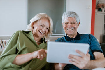 Wall Mural - Happy senior couple at home sitting on couch sharing tablet