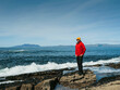 © mark_gusev - A man in a red jacket stands on a rock overlooking the ocean. The man is wearing a yellow hat and he is looking out at the water. The scene is peaceful and serene. West coast of Ireland. Travel theme