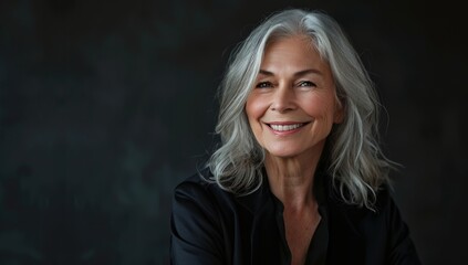 Wall Mural - Elegant middle-aged woman with shoulder-length silver hair, smiling and standing confidently in front of the camera against a black background. senior woman