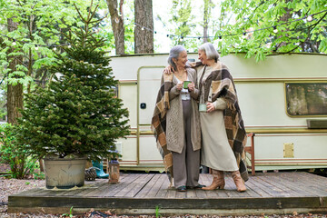 a lesbian couple enjoys a warm drink and a moment together while camping in a forest.