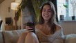 © Pro Hi-Res - Smiling woman uses smartphone while sitting on couch.