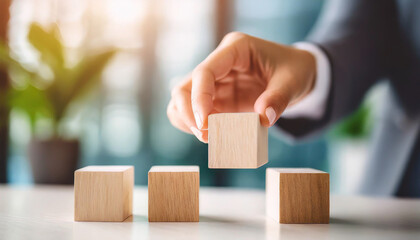 woman's hand places blank blocks in a row on a white surface, with a blurred background of a home, office, or studio. The scene evokes themes of planning, organization, and creativity
