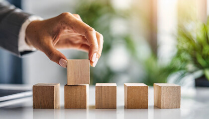 woman's hand places blank blocks in a row on a white surface, with a blurred background of a home, office, or studio. The scene evokes themes of planning, organization, and creativity