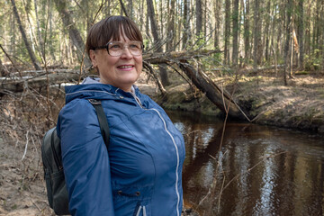 An elderly woman walks along a forest river.