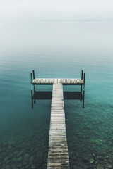 Wall Mural - Aerial view of a solitary pier extending into a calm body of water, emphasizing the clean lines and the contrast between the structure and the natural surroundings. 