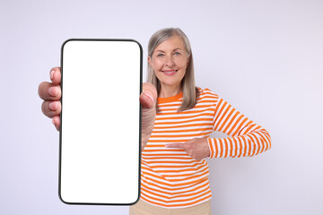 Wall Mural - Happy mature woman showing mobile phone with blank screen on white background. Mockup for design