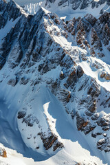 Wall Mural - Aerial view of snowy mountain peaks, highlighting the sharp contrasts between the white snow and the dark rocky outcrops. Focus on the clean lines and dramatic shadows.