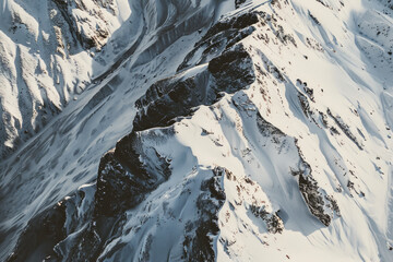 Wall Mural - Aerial view of snowy mountain peaks, highlighting the sharp contrasts between the white snow and the dark rocky outcrops. Focus on the clean lines and dramatic shadows.