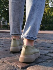 Wall Mural - Close-Up Shot of a Person Wearing Casual Shoes Walking on Cobblestone Street at Dusk