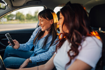 Two cheerful friends sitting in car and looking at GPS on phone.