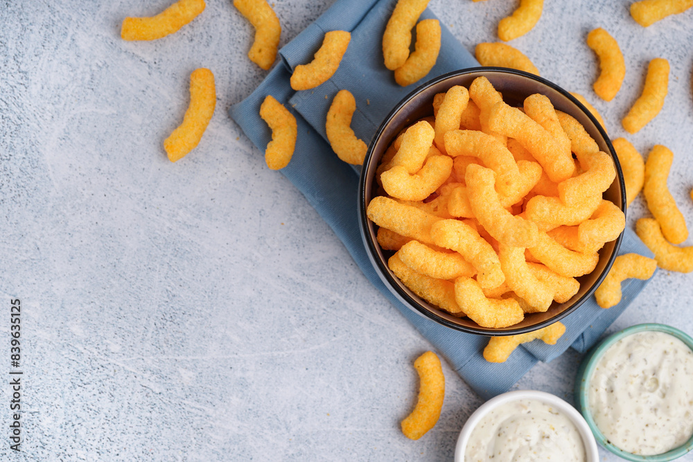 Bowl with tasty salty corn sticks and sauces on light background