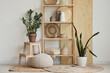 © Pixel-Shot - Shelving unit with statuettes and houseplants near white wall in room