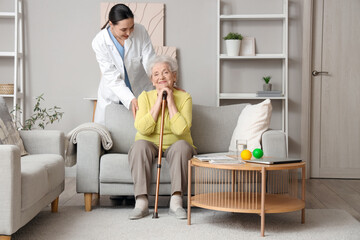 Canvas Print - Senior woman with stick and physical therapist sitting on sofa at home