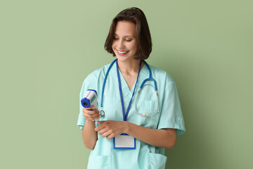 Canvas Print - Beautiful female doctor with infrared thermometer and badge on green background