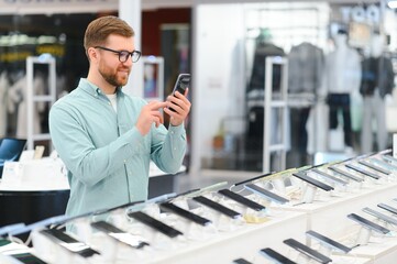 happy young man choosing a new mobile in a tech store