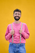 © CarlosBarquero - Vertical. Portrait smiling cheerful young Caucasian man holding his rainbow lgbt suspenders. Gay people posing for photo with yellow background. Cheerful male bearded person happy studio in isolated.