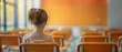 © Naret - A young girl sitting alone in an empty classroom with orange walls and chairs, gazing out the window. Concept of solitude and education.