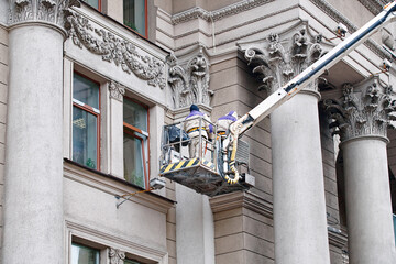 Wall Mural - Utility workers on lift platform, facade restoration on historic building with ornate columns, preservation of urban architecture. Men on lift platform clean and maintain exterior of historic building