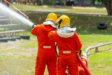 Wall Mural - Firefighter teamwork in fire suit on rescue duty using water from hose extinguishing fighting with big crackle fire flames inside burning premises. Fireman spraying high pressure water fight a fire.