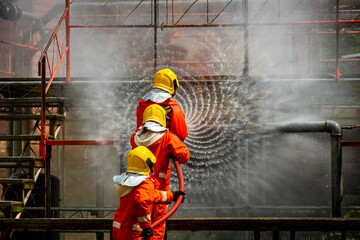 Wall Mural - Firefighters teamwork in fire suit on rescue duty using water from hose extinguishing fighting with big crackle fire flames inside burning premises. Fireman spraying high pressure water fight a fire.