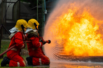 Wall Mural - Firefighters teamwork in fire suit on rescue duty using water from hose extinguishing fighting with big crackle fire flames inside burning premises. Fireman spraying high pressure water fight a fire.