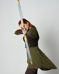 Poster - close up portrait of red haired female model wearing green medieval fantasy costume, leather armour.
Holding archery bow and arrow weapon, standing action pose isolated on white studio background.