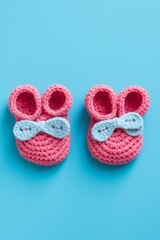 Wall Mural - Two pink baby booties are knitted and placed on a blue background. Concept of warmth and comfort, as the booties are knitted and ready for a baby to wear