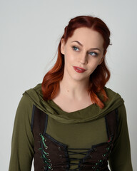 Wall Mural - head and shoulders close up portrait of beautiful red haired female model, wearing  medieval fantasy costume with green tunic  and brown bodice. isolated on studio background
