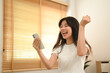© Prathankarnpap - Excited young asian woman reading good news on mobile phone celebrating with yes gesture