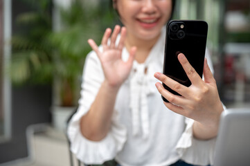 A woman talking on a video call on her smartphone while sitting at an outdoor table of a cafe.