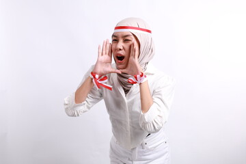 Young beautiful muslim woman wearing red white flag ribbon shouting and screaming loud with a hand on her mouth. Indonesia's independence day concept.