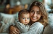 © yevgeniya131988 - Mother joyfully sitting on sofa holding her baby boy in living room, wearing a white shirt