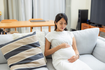 Poster - Pregnant woman sit on sofa and look at her tummy