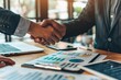 © Sandu - Two men shaking hands desk laptops papers