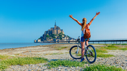 Wall Mural - Happy woman tourist in bicycle enjoying view of Mont Saint Michel, France, Normandy