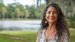 © Антон Сальников - An elegant latina woman in her 50s who exudes happiness in a beautiful natural location near a lake, a genuine smile on her face, relaxed and confident, a latin woman who has found happiness