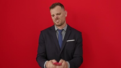 Wall Mural - Furious young hispanic man in suit, shouting angrily over smartphone, enraged and frustrated, radiating rage and aggression on isolated red background