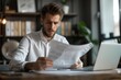 © Sandu - Man reads paper at desk with laptop