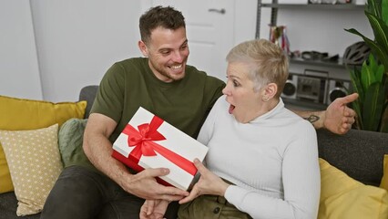 Wall Mural - A woman and man share a joyful moment with a gift in a cozy living room, expressing happiness and surprise.