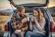 © Tatiana Sidorova - Couple sitting in the open car trunk enjoy a cup of coffee during  a road trip