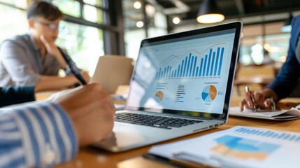 Poster - A person takes notes on a notebook while viewing data analysis graphs on their laptop computer.