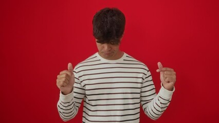 Canvas Print - Young hispanic man wearing stripes t-shirt standing, pointing down, looking sad, unhappy, upset, indicating direction with finger, over isolated red background, feeling depressed and displeased