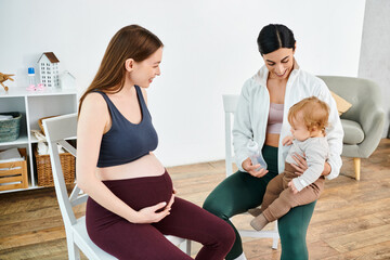 Wall Mural - A pregnant woman sits gracefully on a chair, cradling a baby in her lap with the support of her coach at parents courses.