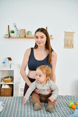 Wall Mural - A young, beautiful mother gently cradles her baby while sitting on a cozy bed at home, parents courses.