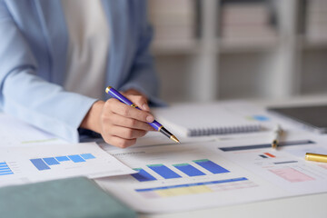 Close-up of a person's hand analyzing financial charts and graphs at a desk in an office setting, symbolizing business strategy and data analysis.