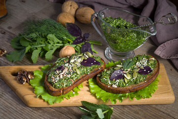 Toasts with homemade pesto sauce with sunflower seeds, sesame seeds and basil leaves on a wooden serving board