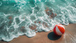 © NaphakStudio - A beach ball on the sandy shore, with turquoise waves gently washing over it, capturing a refreshing summer moment.