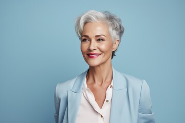 Wall Mural - Portrait of a jovial woman in her 50s dressed in a stylish blazer while standing against pastel blue background