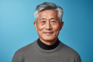 Wall Mural - Portrait of a tender asian man in his 60s dressed in a warm wool sweater isolated on pastel blue background